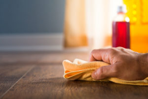 Male hand applying wood care products and cleaners on hardwood floor surface.